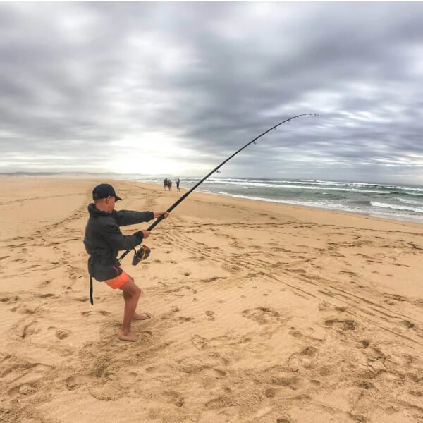 Things to Do in Jeffreys Bay, Surf Fishing, Man reeling in a big fish off the beach.